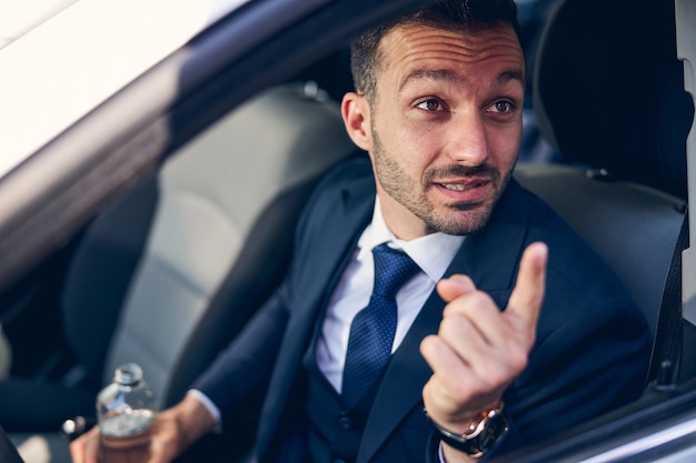 Handsome brunette male person wrinkling forehead while actively gesticulating during conversation, sitting in his auto