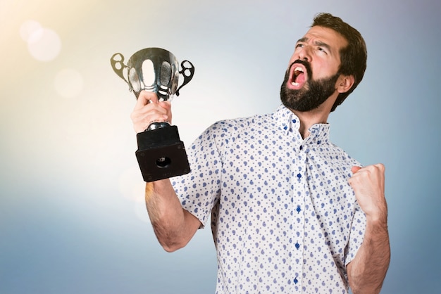 Uomo castana bello con la barba che tiene un trofeo