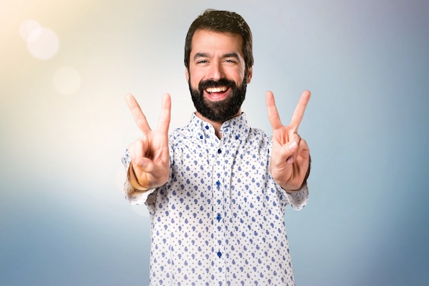 Uomo castana bello con la barba che fa gesto di vittoria