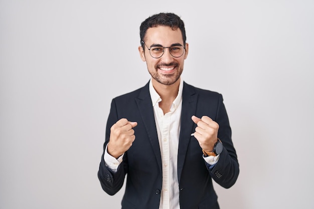 Photo handsome business hispanic man standing over white background very happy and excited doing winner gesture with arms raised, smiling and screaming for success. celebration concept.