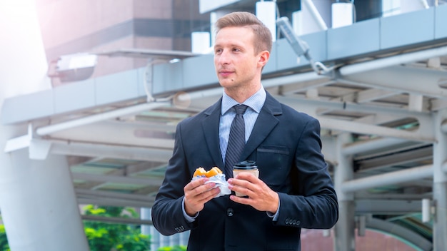 Handsome business man eating breakfast fastfood hamburger and drinking cup of coffee