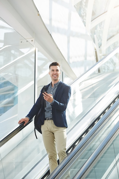 Handsome business man on escalator smiling with smart phone