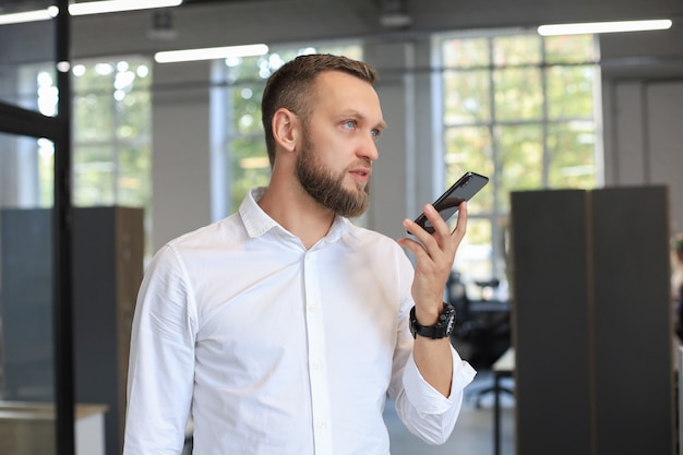 Handsome business man using a voice recognition app in office.