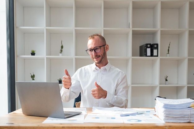 Handsome business man working using computer and paper happy with big smile doing thumb up with fingers excellent sign