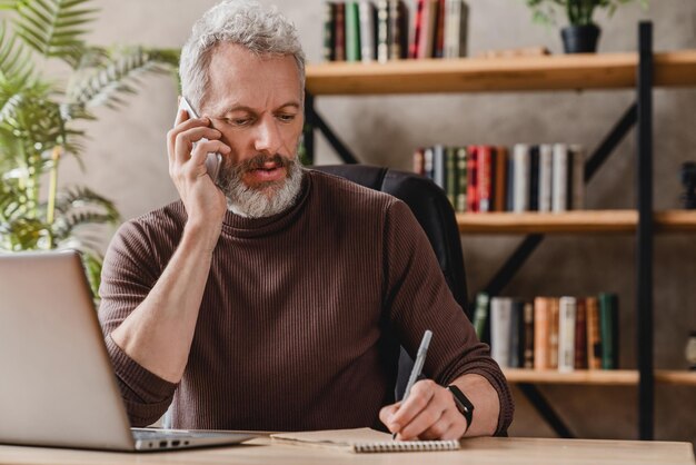 Handsome businessman in casual clothes talking on mobile phone and making notes