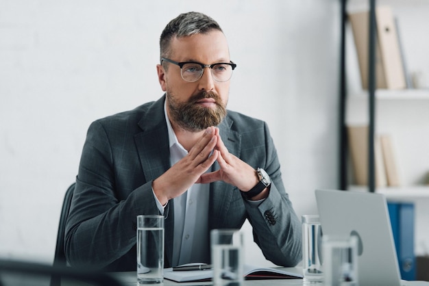 Handsome businessman in formal wear and glasses looking away in office