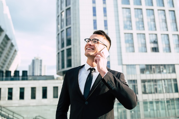 Handsome businessman in full black suit talks on his smart\
phone at the cityscape background