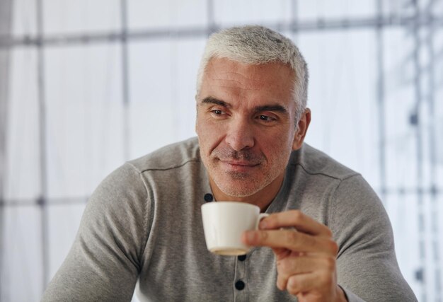 Uomo d'affari bello che mangia tè o caffè in ufficio