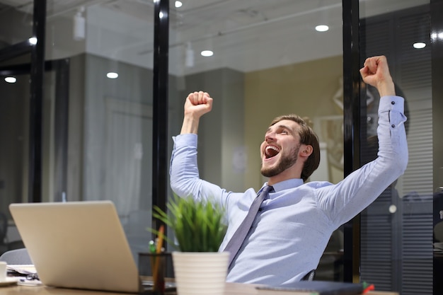 Handsome businessman is keeping arms raised and expressing joyful in office.