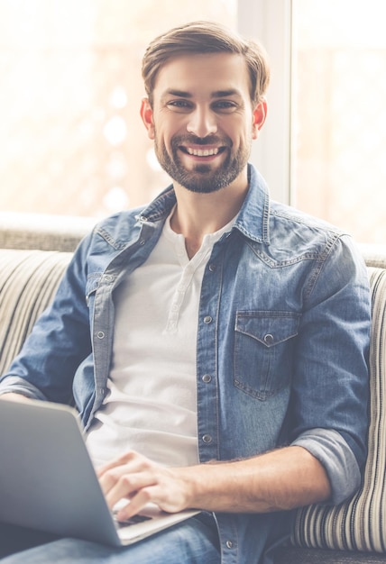 Handsome businessman is looking at camera and smiling while working with a laptop at home