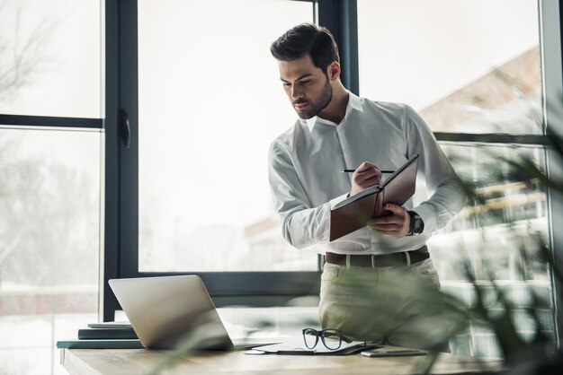 Handsome businessman is making notes while working with a laptop in the office