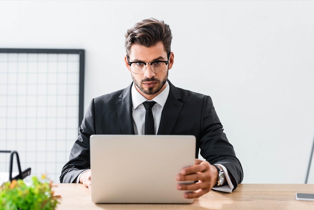 Handsome businessman looking at camera while using laptop