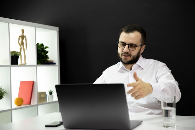 Handsome businessman pointing to monitor, talks online by webcam, remote work