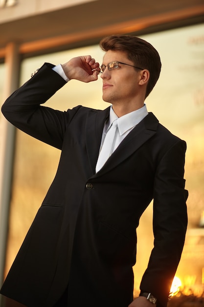 Handsome businessman posing in eyeglasses and black suit, wear watch on his hand.