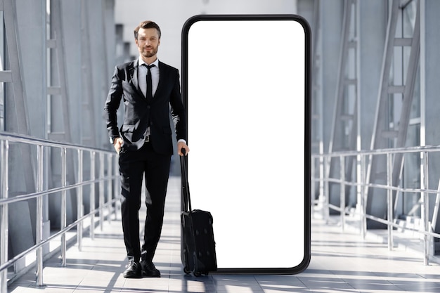 Handsome businessman in suit with suitcase standing by huge smartphone