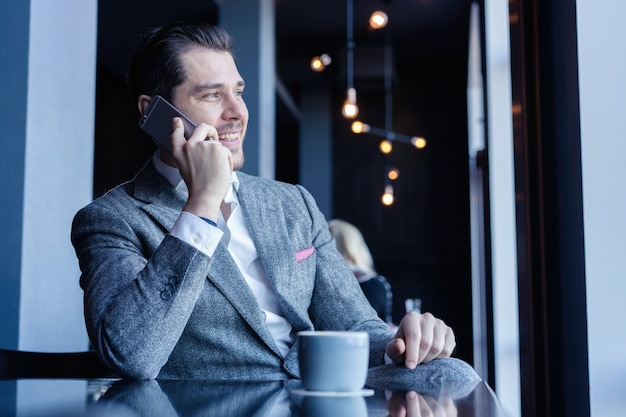 Handsome businessman talking on the phone in cafe and looking away