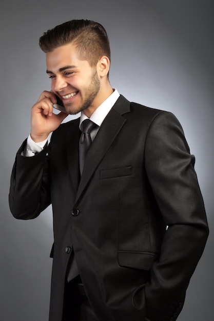 Handsome businessman talking on phone on gray background