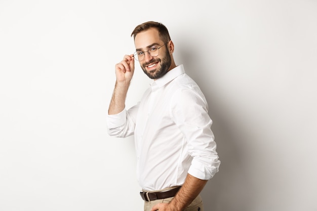 Handsome businessman turn at camera and looking confident, smiling cheeky, standing over white background.