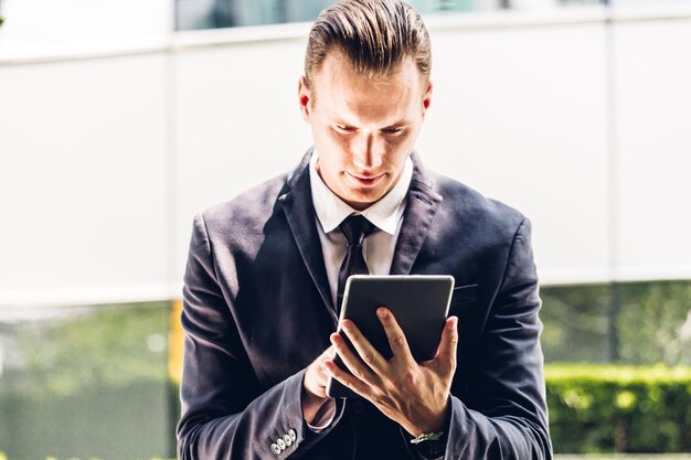 Photo handsome businessman using digital tablet while sitting against building