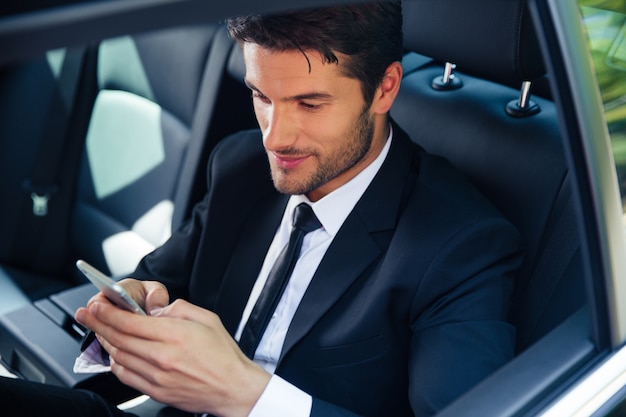 Bell'uomo d'affari che utilizza lo smartphone in auto