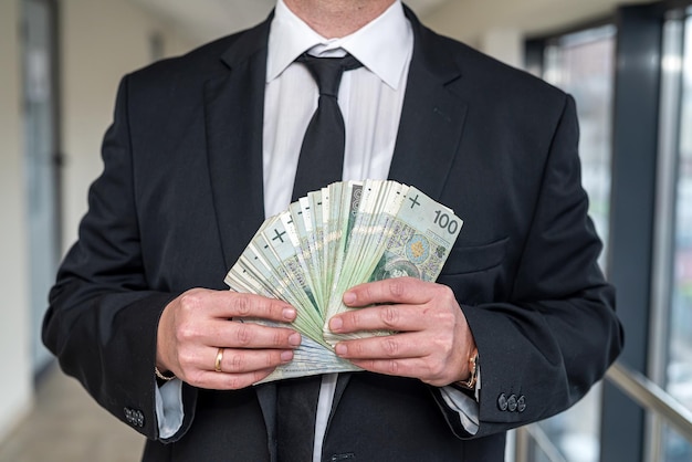 Handsome businessman who earns a lot holds zlotys in his hands to invest money