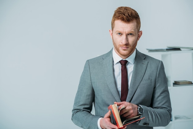 Handsome businessman with book standing in office