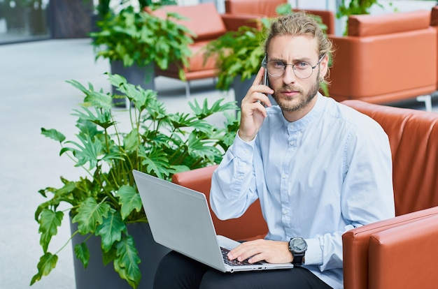 A handsome  businessman works on a laptop and speaks on the phone sitting in a modern off