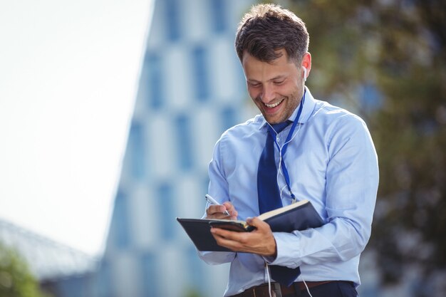 Handsome businessman writing in dairy while listening music