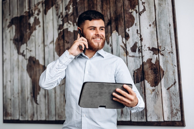 Handsome busy businessman talking on the phone and looking at important document on tablet.