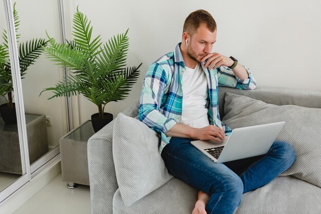 Handsome busy focused man in shirt sitting relaxed on sofa at home at table working online on laptop from home