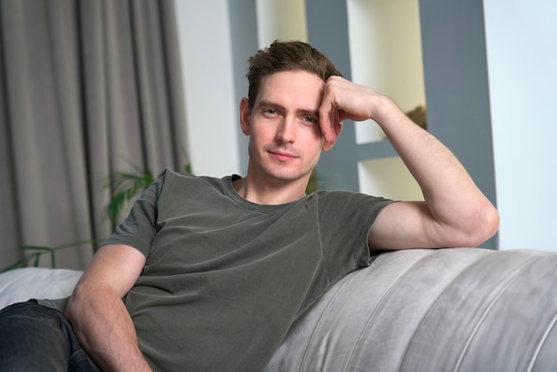 Handsome calm relaxed man is sitting on couch or sofa at home in living room looking at camera