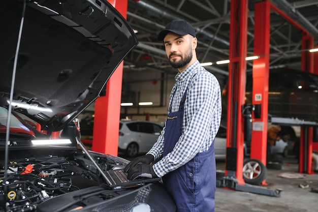 ハンサムな自動車整備士が車のサービスでポーズをとっています。