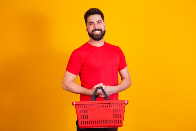 Handsome caucasian boy holding a shopping basket on yellow background. shopping concept