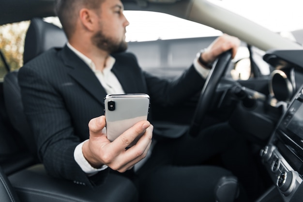 Handsome caucasian businessman driver inside in vehicle  with gadget and check mail and talking with partners