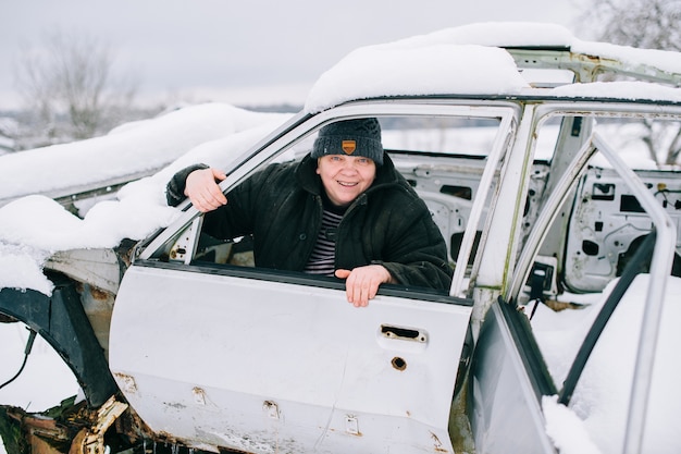 Handsome caucasian chubby woman in warm clothes sits in old white car in village