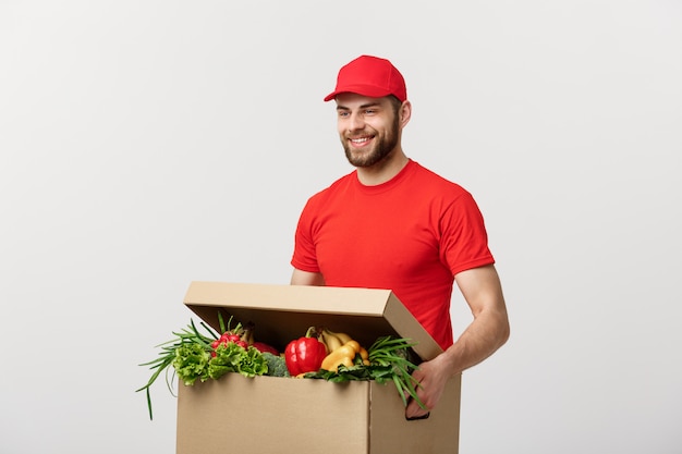 Handsome Caucasian grocery delivery courier man in red uniform with grocery box with fresh fruit and vegetable