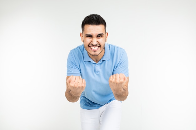 Handsome caucasian man in a blue t-shirt holds fists for good luck on a white studio