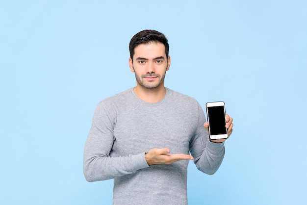 Handsome Caucasian man showing mobile phone with empty screen isolated on light blue background