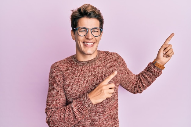 Handsome caucasian man wearing casual sweater and glasses smiling and looking at the camera pointing with two hands and fingers to the side.