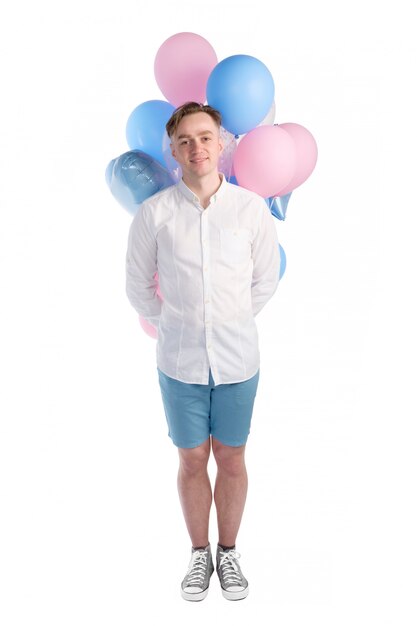 Handsome caucasian man in white shirt laughing and holding pink and blue balloons behind back isolated