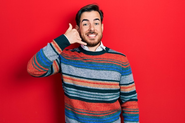 Handsome caucasian man with beard wearing elegant wool winter sweater smiling doing phone gesture with hand and fingers like talking on the telephone communicating concepts