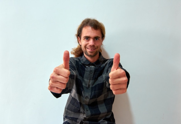 A handsome caucasian man with long hair showing a thumbs up with both hands on a white background