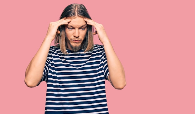 Handsome caucasian man with long hair wearing casual striped tshirt with hand on head for pain in head because stress suffering migraine