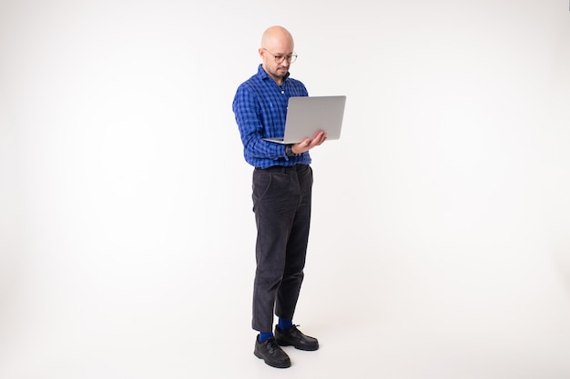 Handsome caucasian man without hair in blue shirt, black trousers and blue socks works with laptop