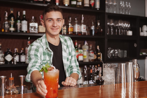 Handsome cheerful bartender enjoying working at his bar, serving delicious cocktail, copy space