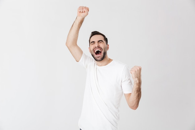 Handsome cheerful man wearing blank t-shirt standing isolated over white wall, celebrating success