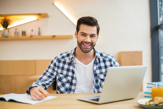 Handsome cheerful nice man sitting in front of his laptop and smiling while working in the office