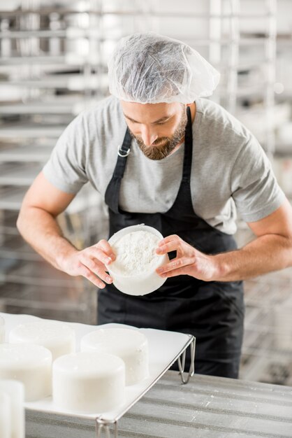 Handsome cheese maker in uniform forming cheese into molds at the small producing farm