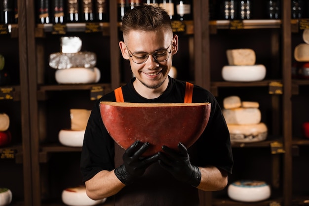 Handsome cheese sommelier holding and jokes with limited gouda cheese Snack tasty piece of cheese for appetizer Hungry man