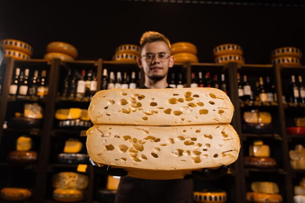 Handsome cheese sommelier with 2 half of yellow cheese wheel
limited maasdam natural aged cutting cheese in store big pieces of
cheese in hands